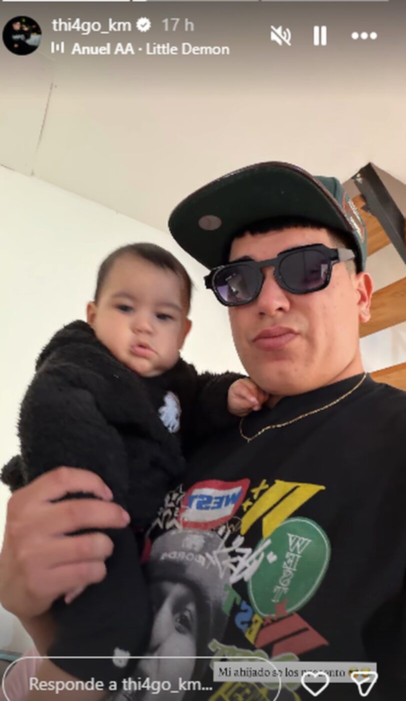 Thiago Medina sosteniendo a un bebé en brazos con gafas de sol y gorra