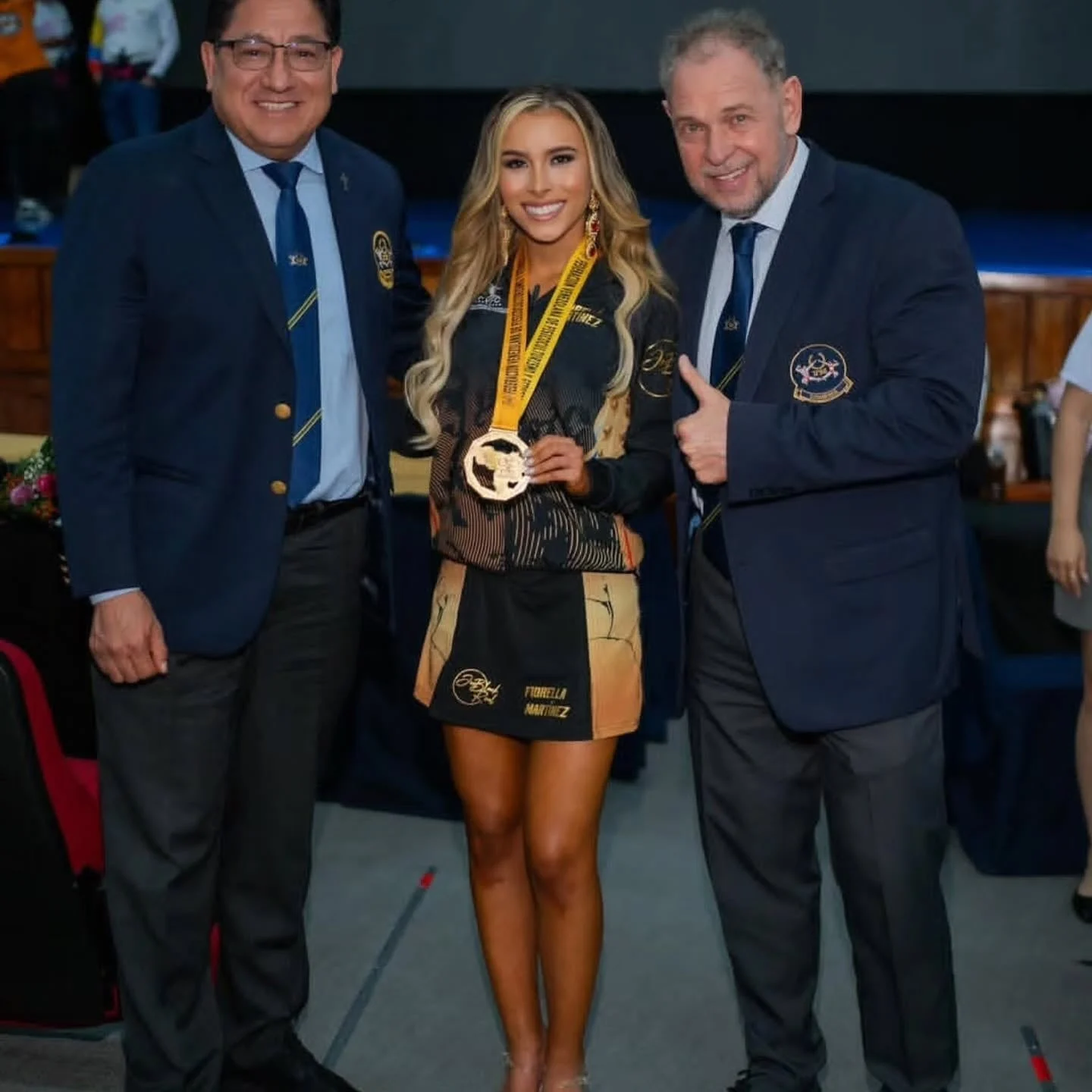 Fiorella Martínez, joven fisicoculturista venezolana, posando con medalla junto a dos hombres en un evento deportivo