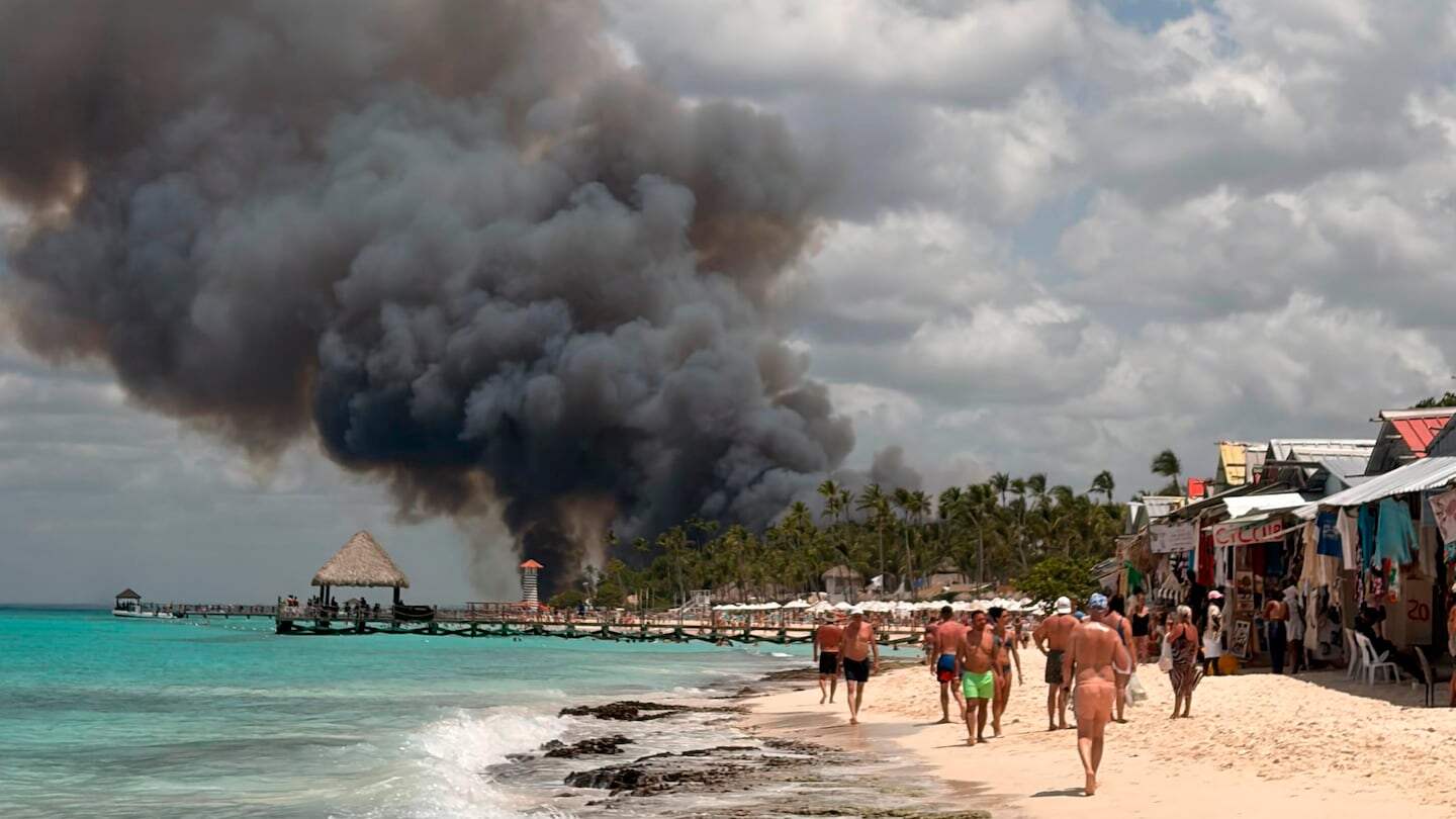 Humo negro se eleva sobre el hotel Viva Wyndham Dominicus Beach en República Dominicana mientras turistas caminan por la playa