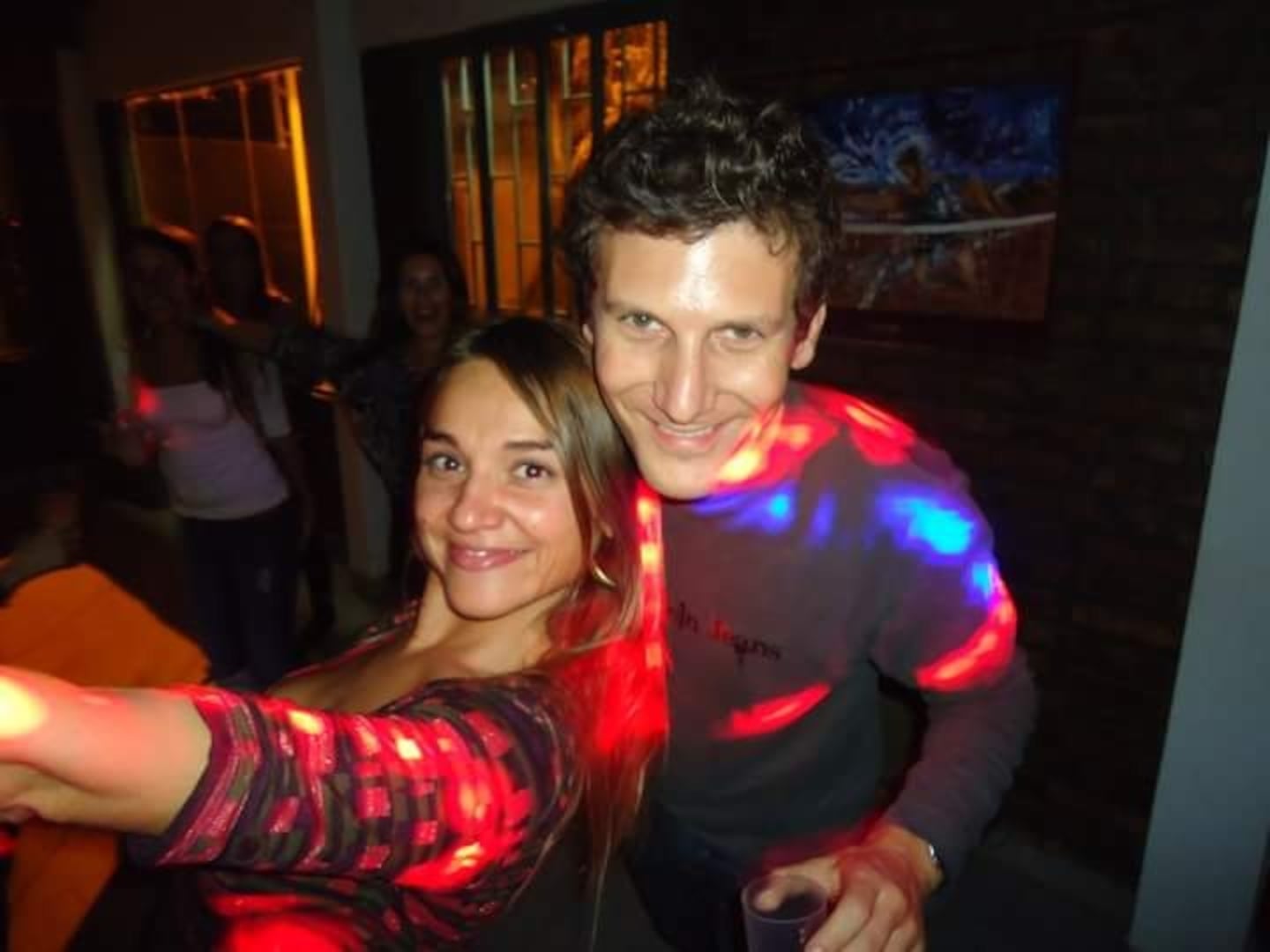 Ana Paula y Julio sonríen juntos en una fiesta con luces de colores