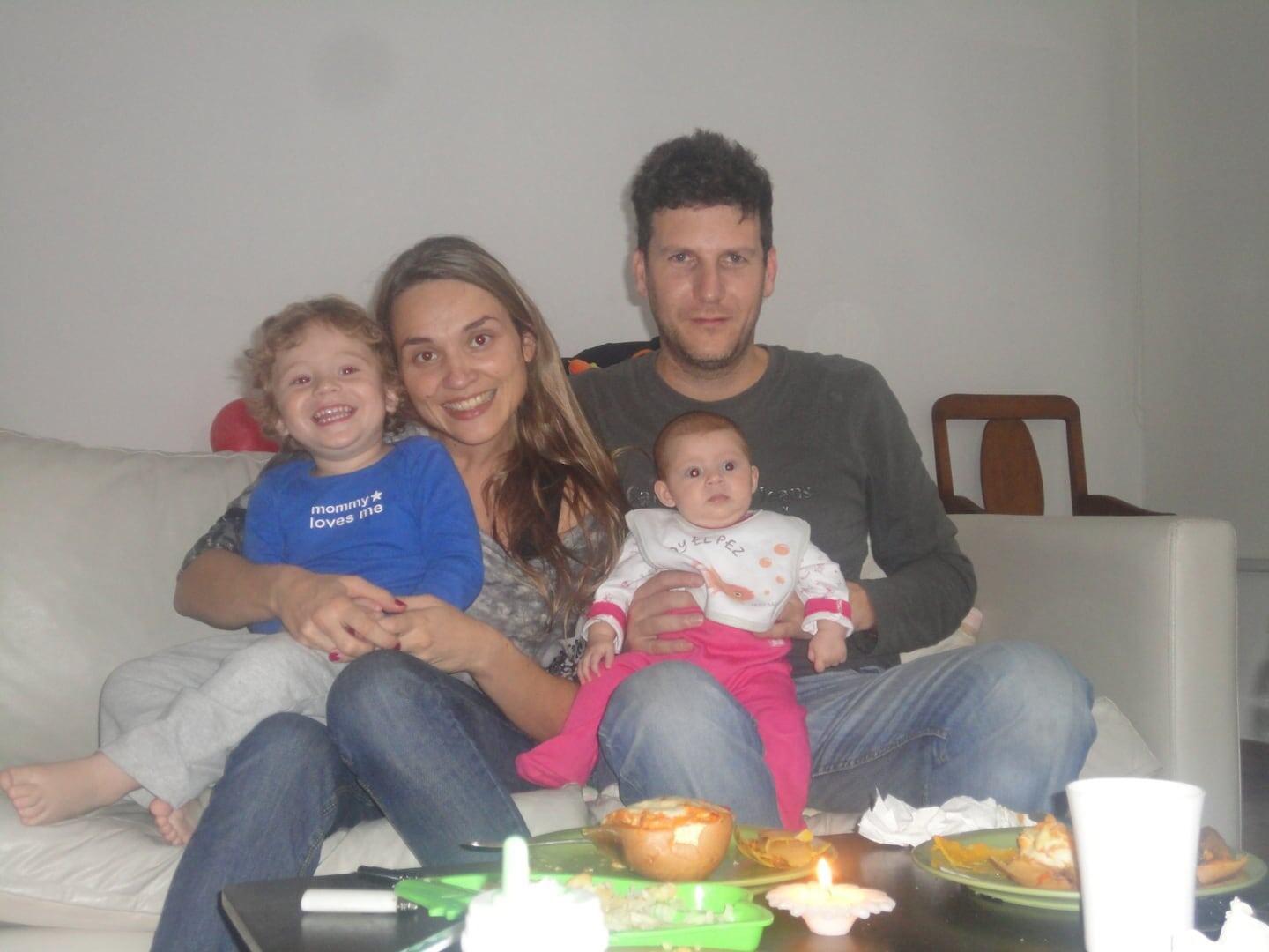 Familia sonriente sentada en un sofá, con dos niños pequeños en brazos y comida en la mesa