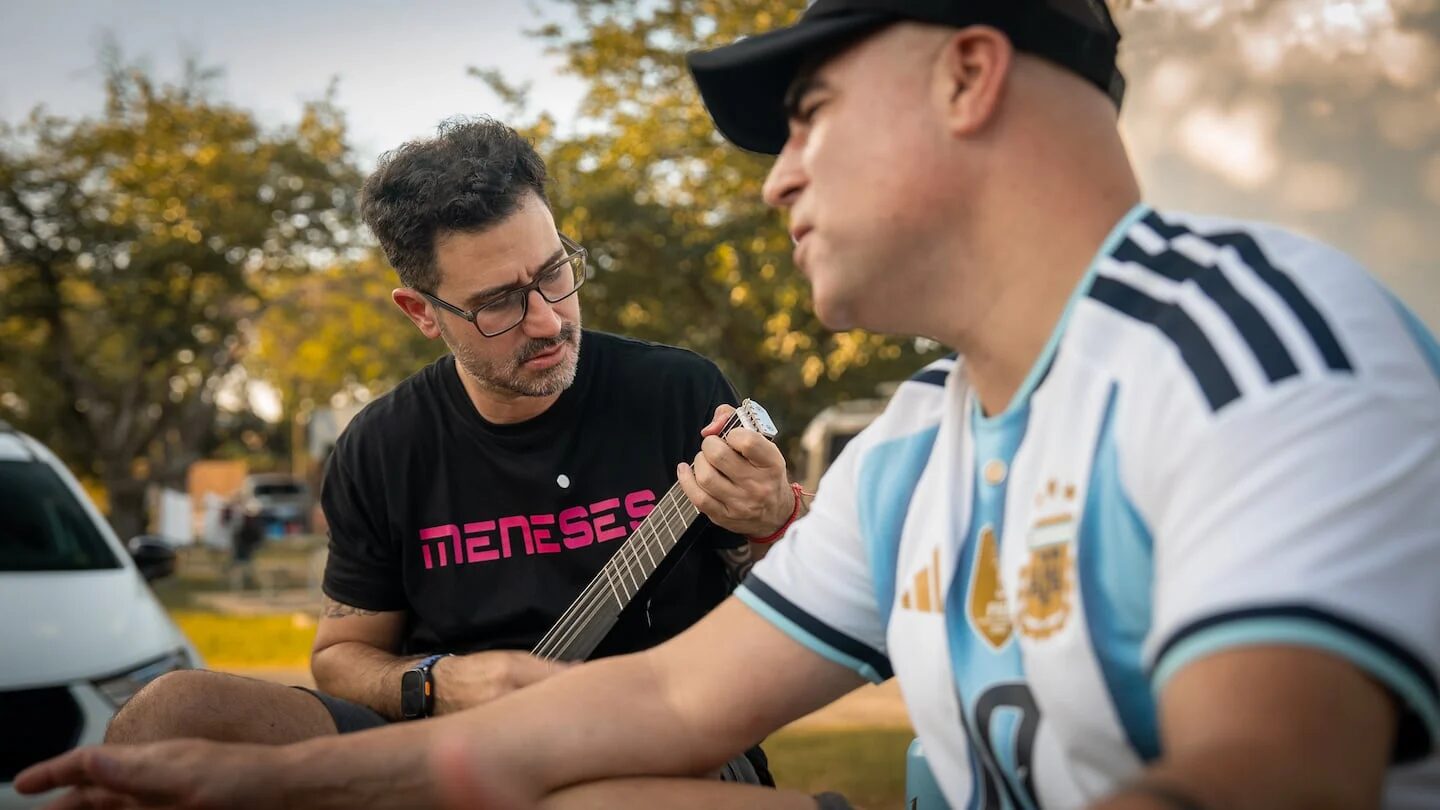 Santiago Meneses tocando la guitarra junto a un amigo en un ambiente al aire libre