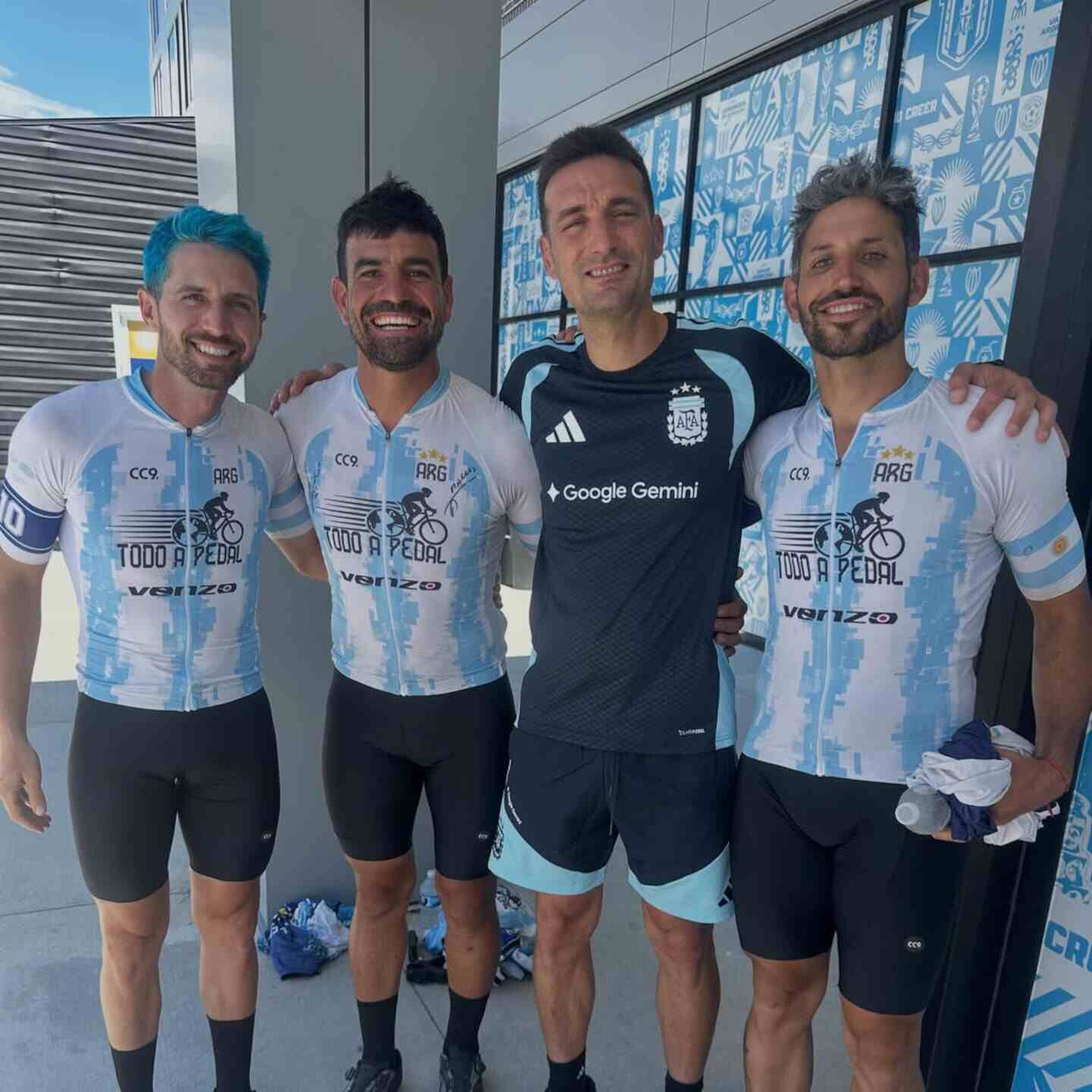 Cuatro hombres sonrientes posan juntos, uno de ellos con camiseta de la selección argentina de fútbol