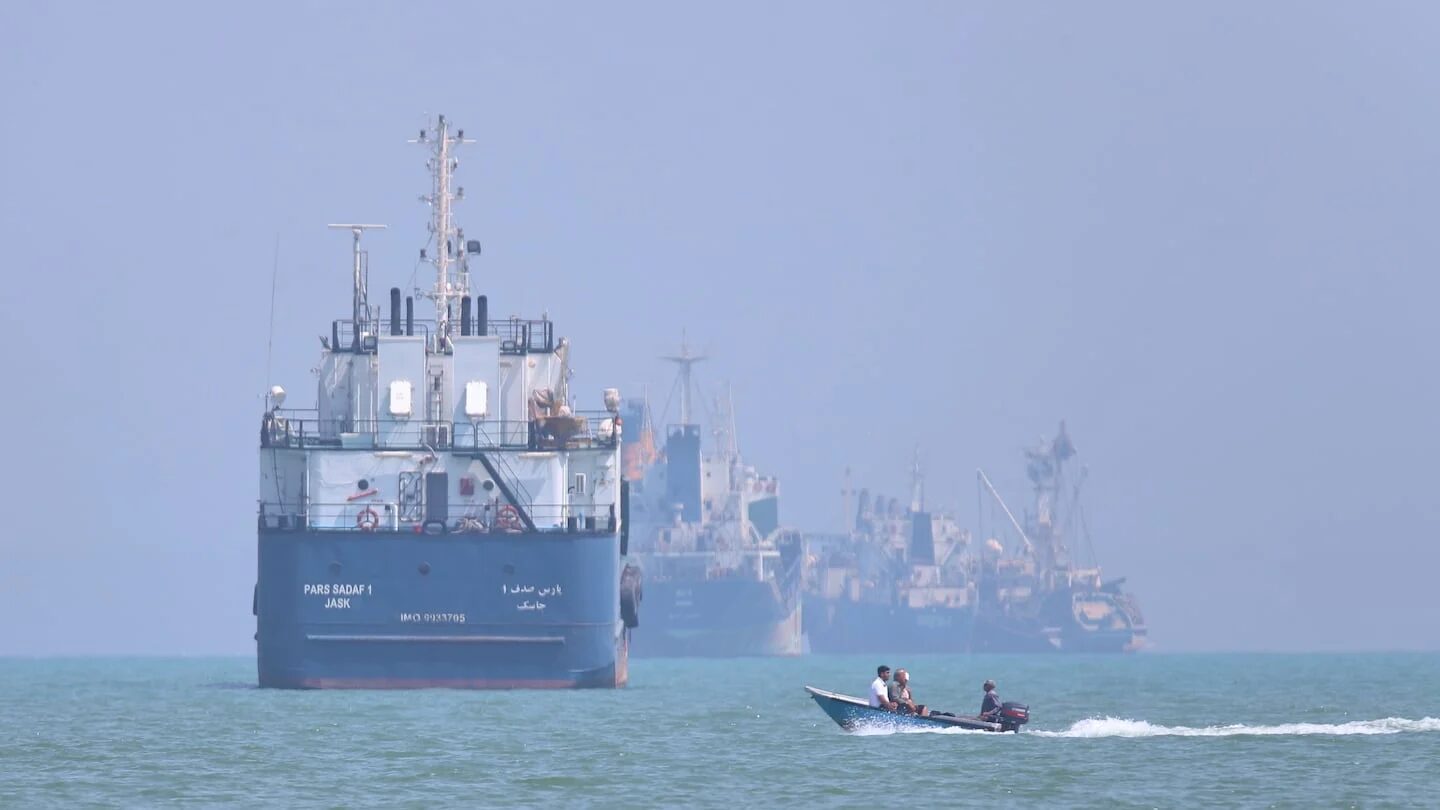 Barco de carga y embarcaciones pequeñas en el mar, simbolizando tensiones navales entre EE.UU. e Irán