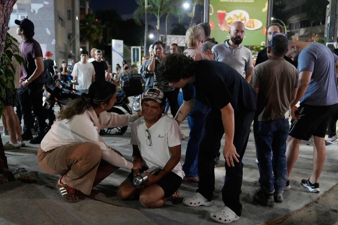 Grupo de personas en la calle tras un terremoto en Venezuela, con un hombre sentado y otros apoyándolo