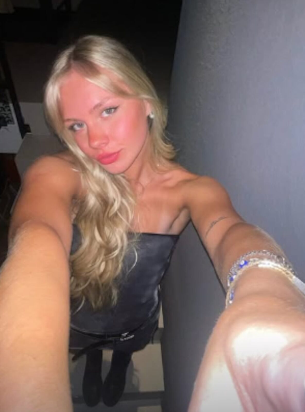Mujer rubia con blusa negra posando para una selfie en un entorno interior