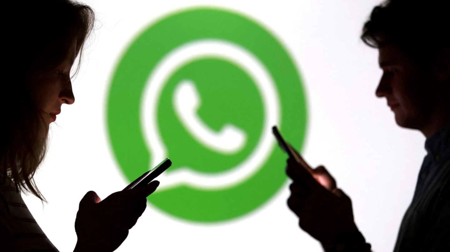 Silhouette de dos personas usando teléfonos móviles frente al logo de WhatsApp