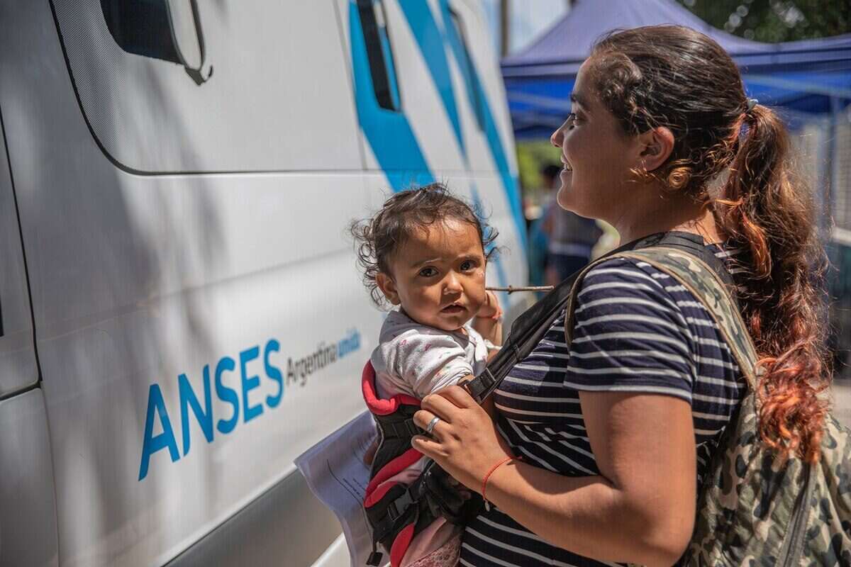 Mujer con un bebé en brazos frente a un vehículo de ANSES
