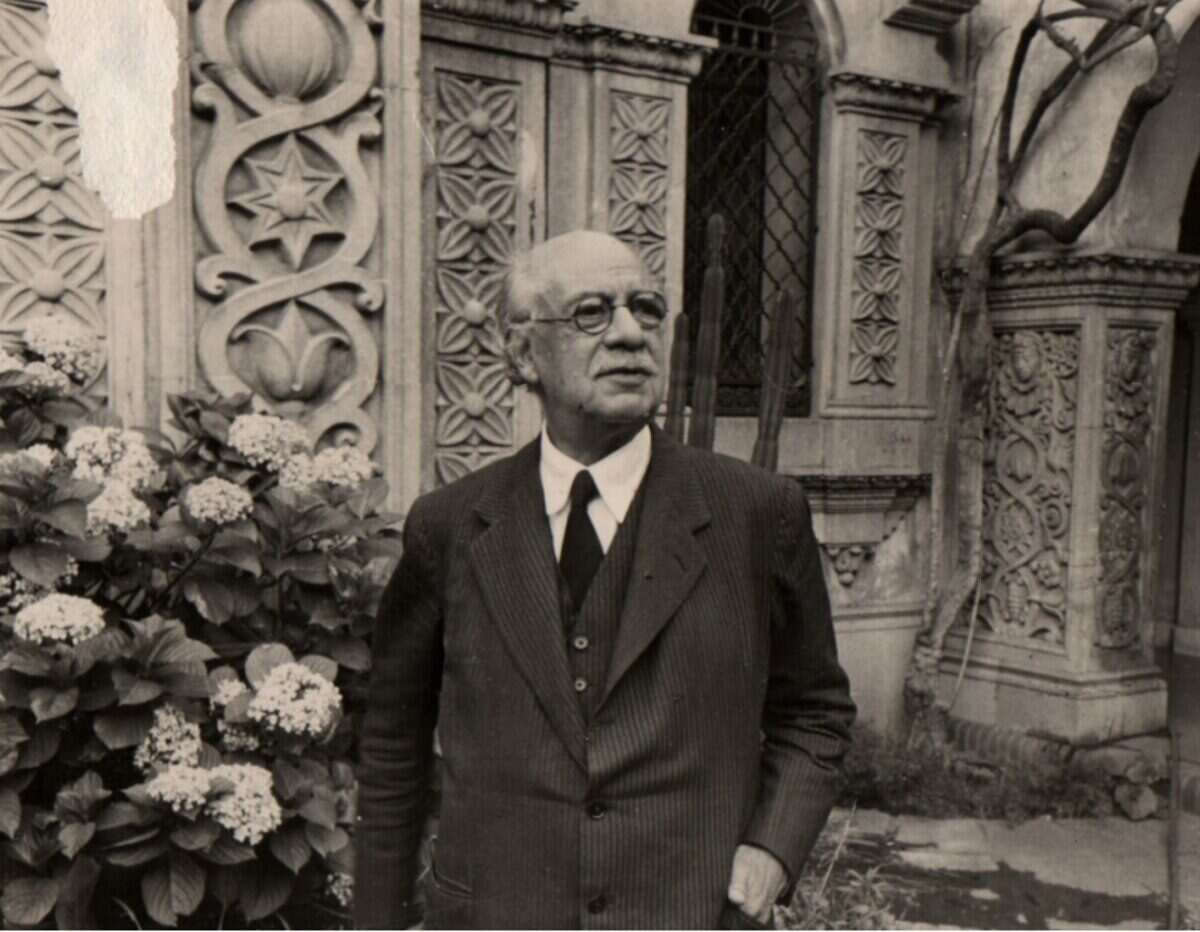 Ricardo Rojas posando frente a un edificio ornamentado con flores en primer plano