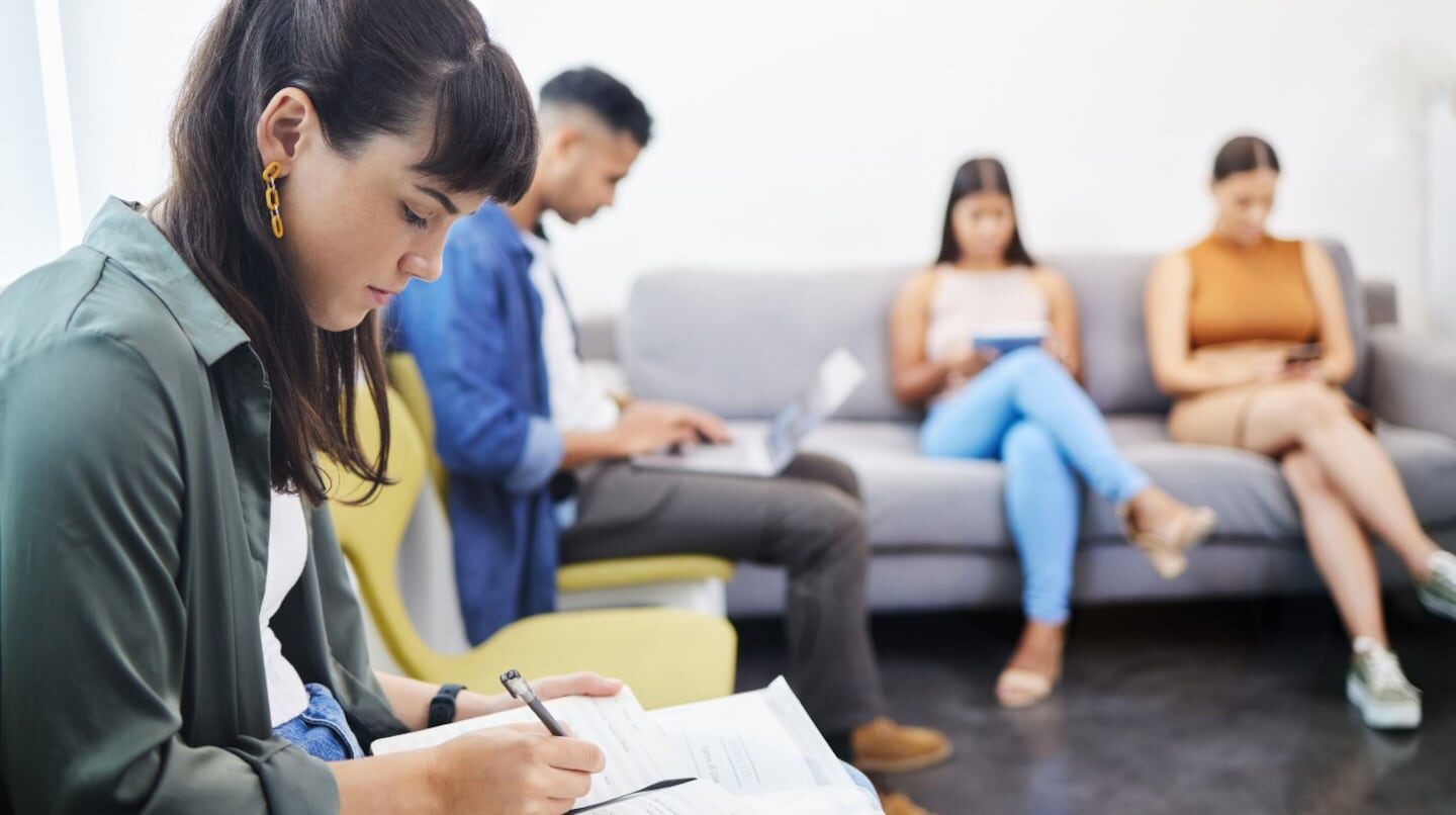 Personas esperando en una sala de espera, una mujer escribe en un cuaderno