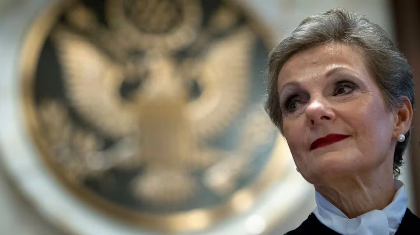 Mujer con cabello corto y maquillaje elegante frente al sello del gobierno de Estados Unidos