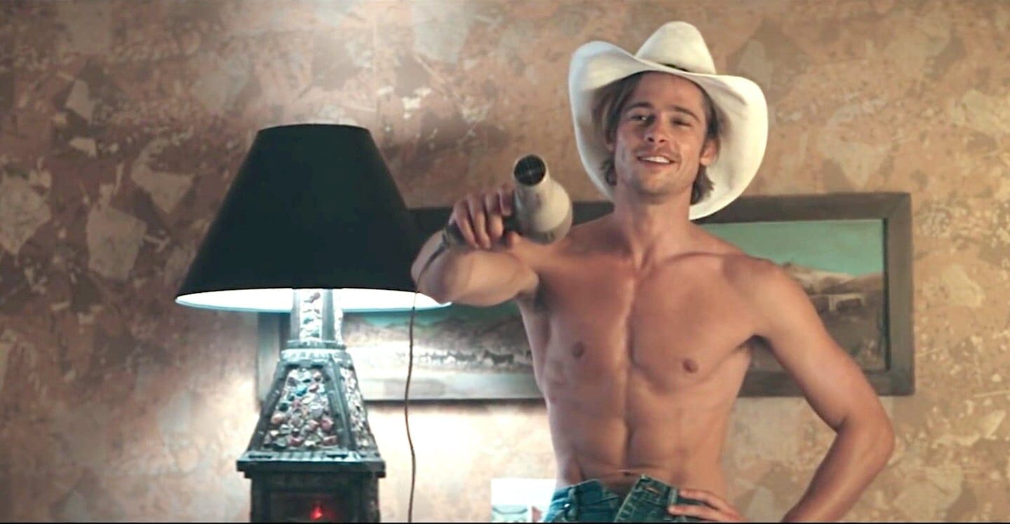 Brad Pitt con sombrero de vaquero y sin camiseta, sosteniendo un secador de pelo