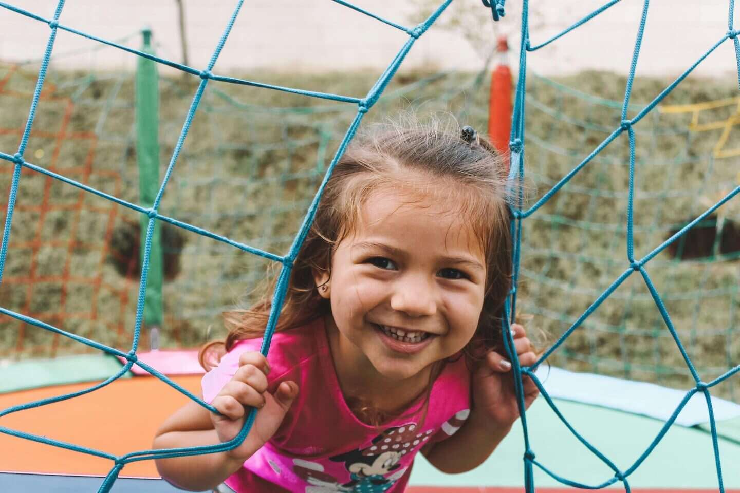 Niña sonriendo mientras juega en una red de escalada en un parque