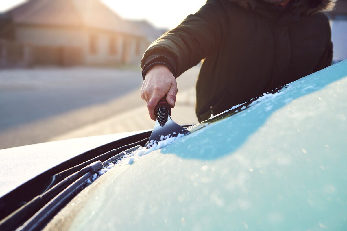 Persona raspando el hielo del parabrisas de un automóvil en invierno