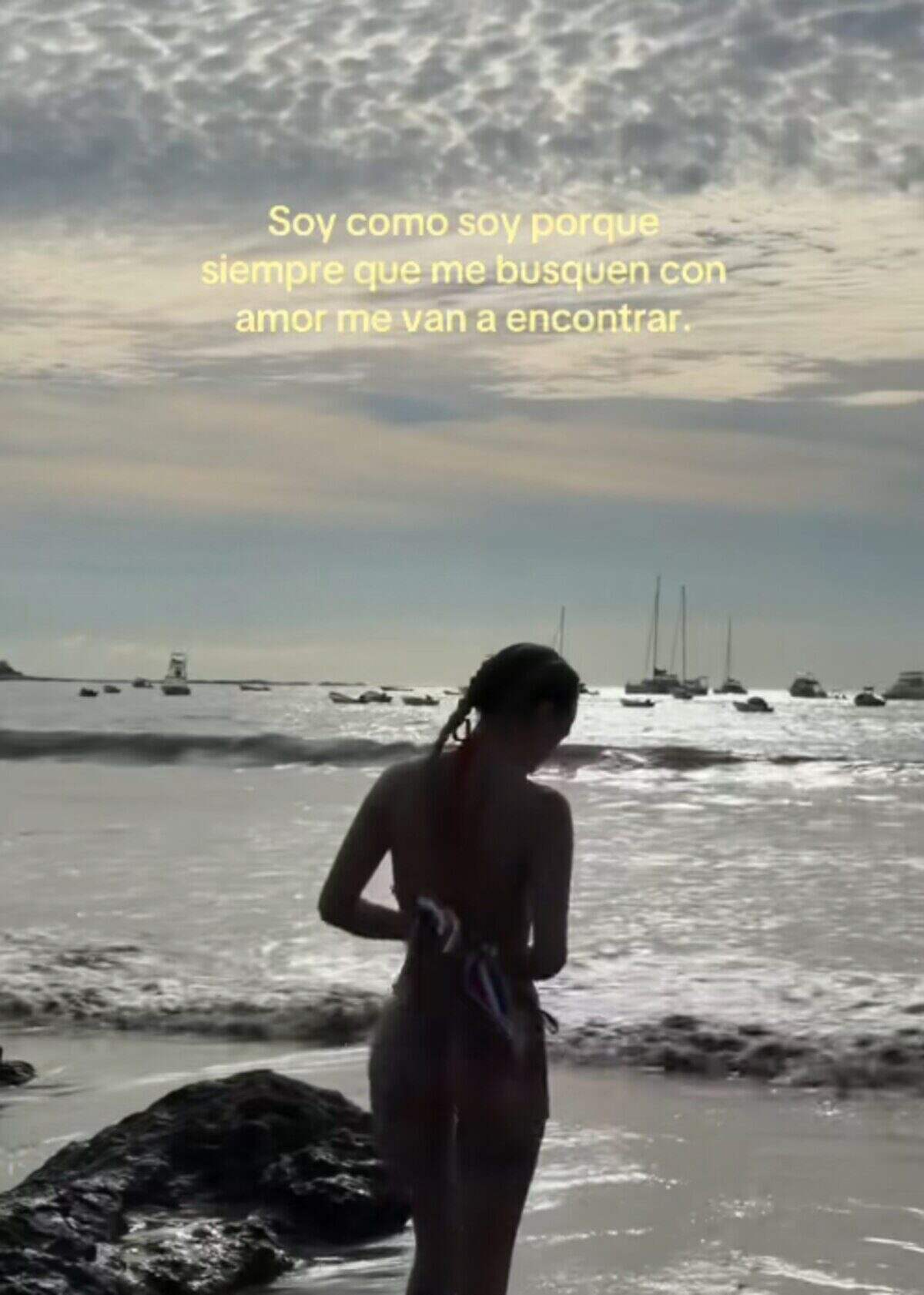 Mujer de espaldas en la playa al atardecer, con un mensaje inspirador en el cielo