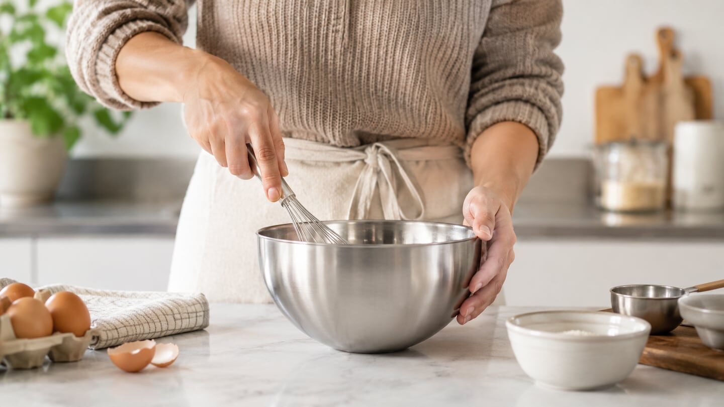 Persona usando un batidor en un bowl de acero inoxidable en la cocina