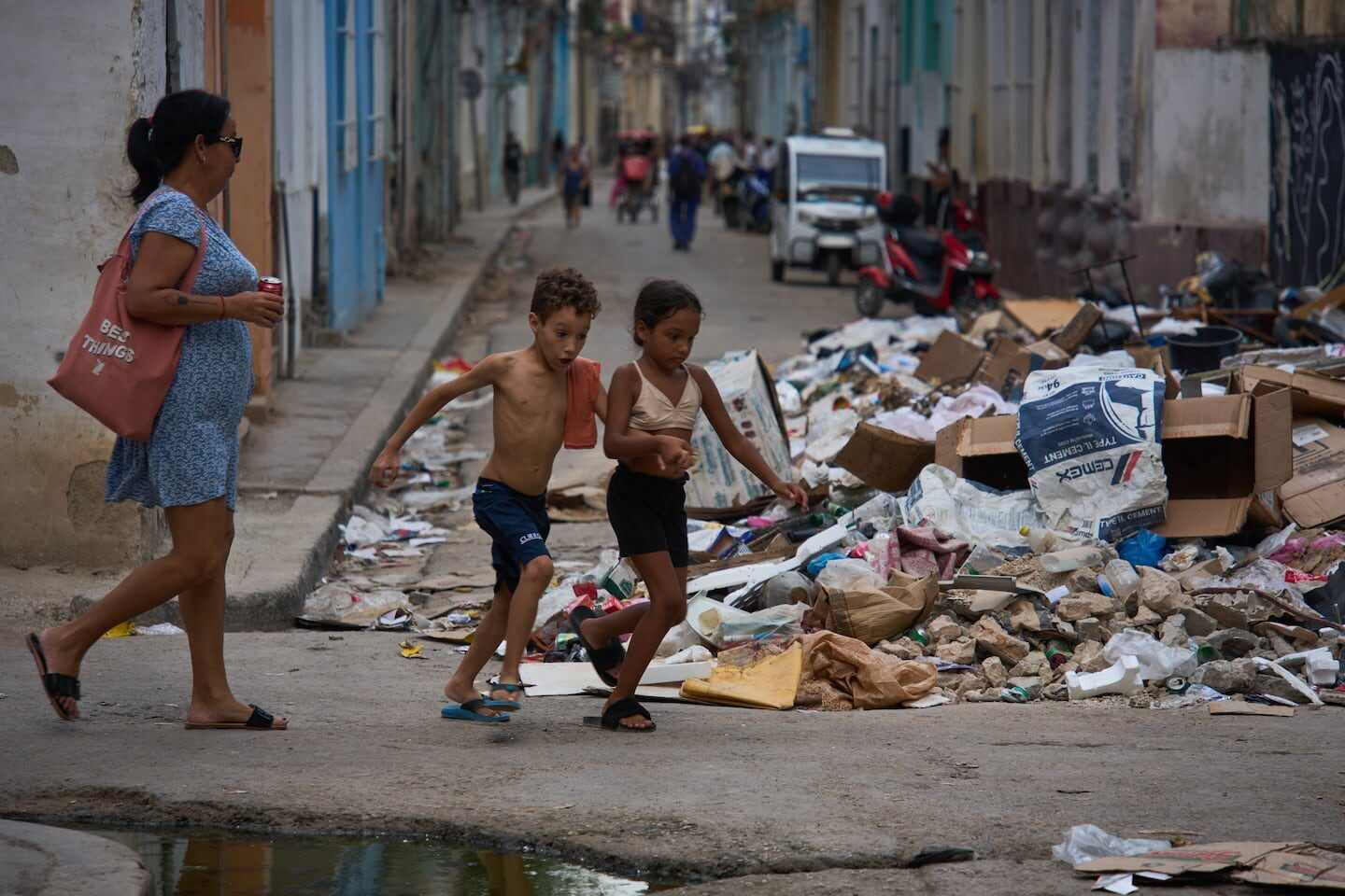 Una mujer camina junto a dos niños en una calle de Cuba con basura acumulada