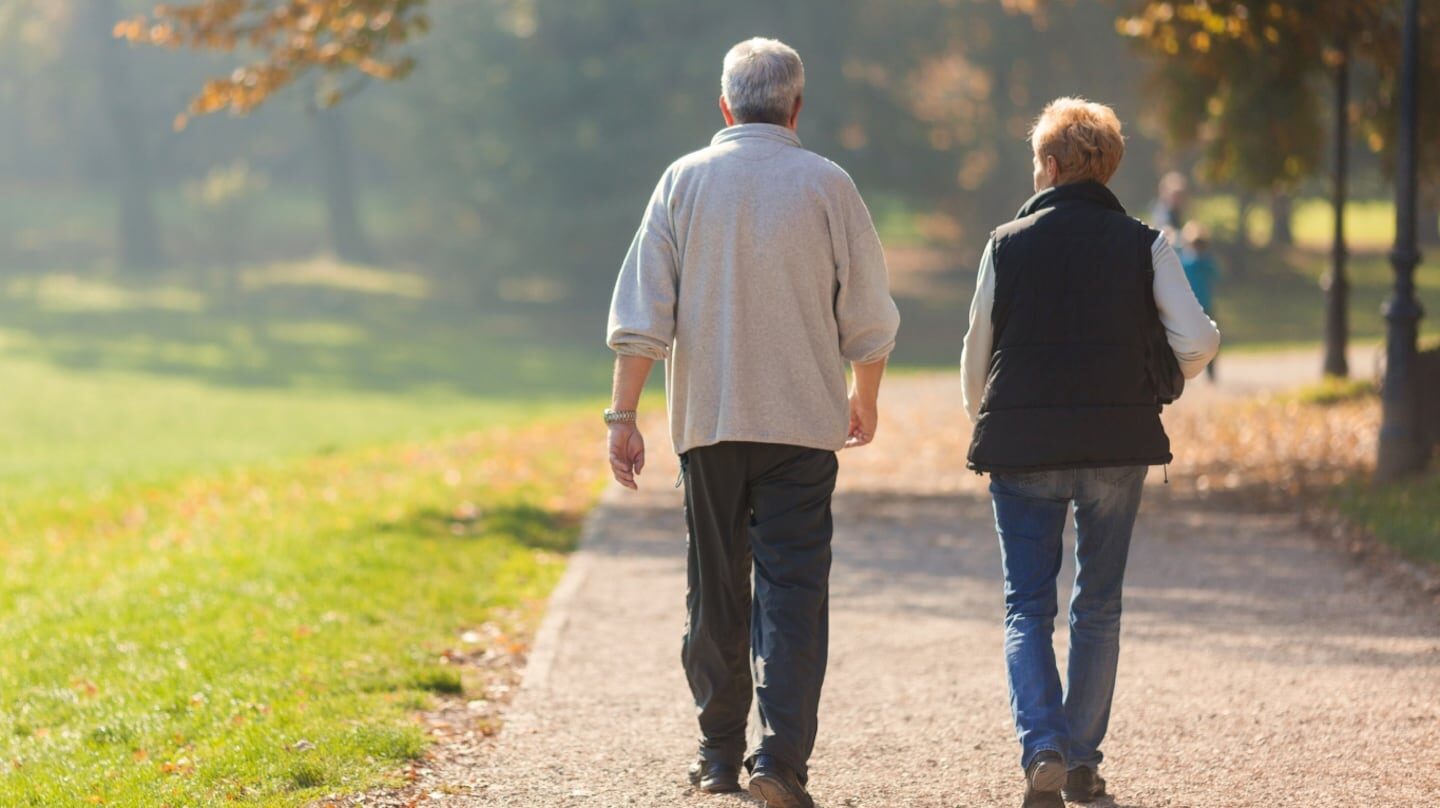Pareja de adultos mayores caminando por un parque en un día soleado
