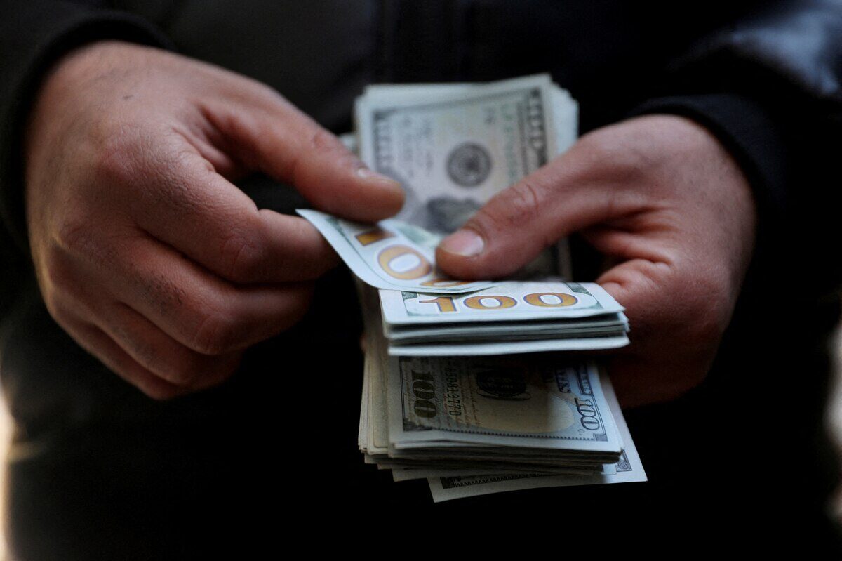 Manos sosteniendo billetes de 100 dólares en un entorno urbano