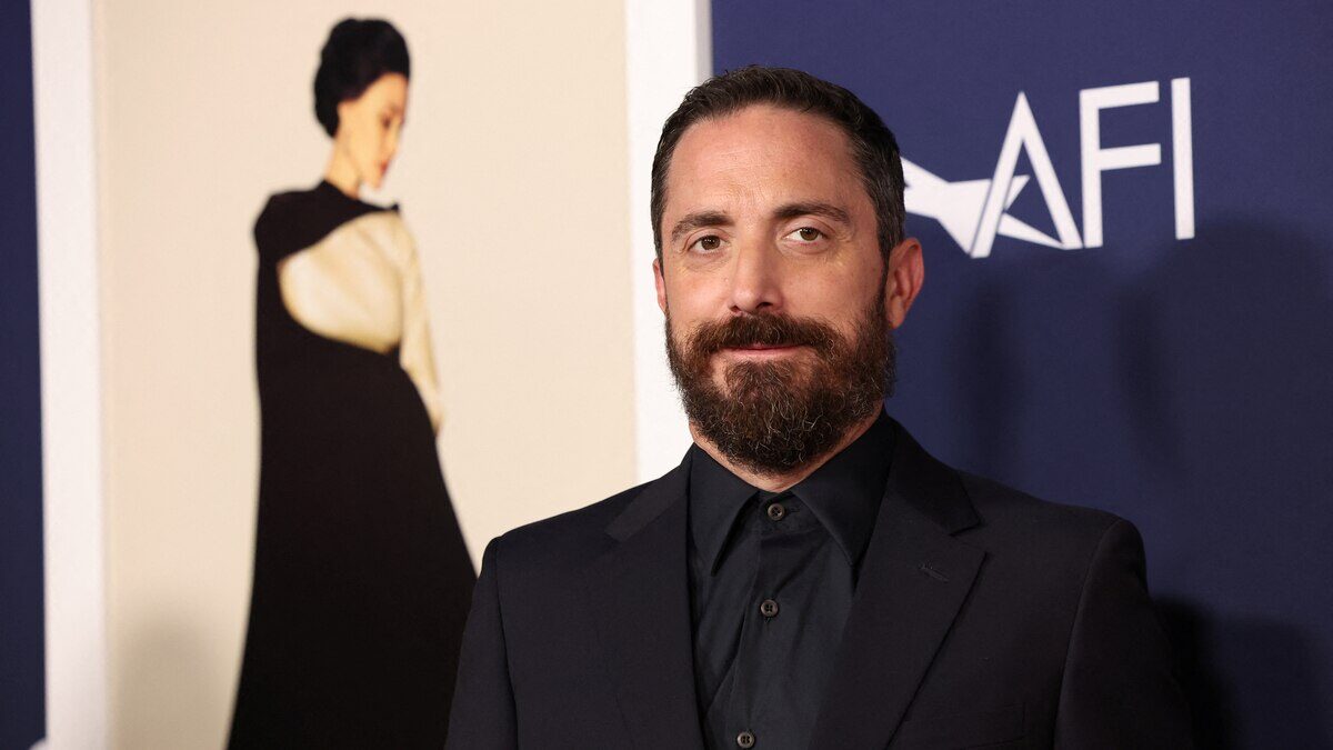 Hombre con barba y traje oscuro posando frente a un fondo con una imagen artística