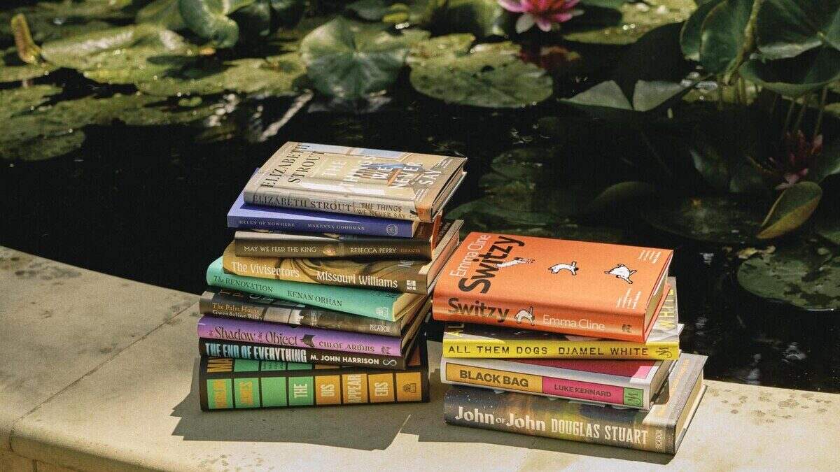 Pila de libros de autores destacados como Douglas Stuart y Marlon James sobre una superficie junto a un estanque