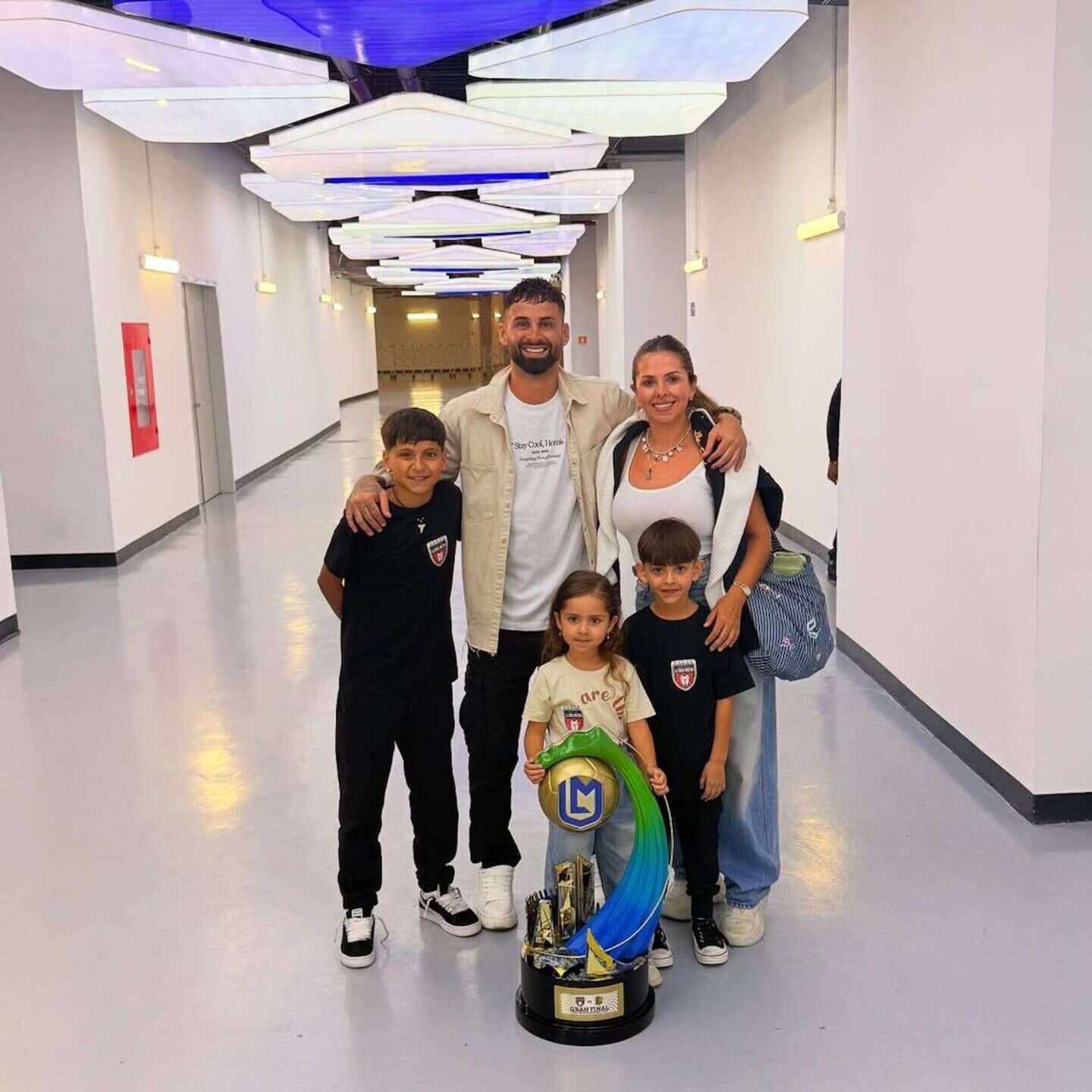 Lucas Trejo posando con su familia y un trofeo en un pasillo iluminado