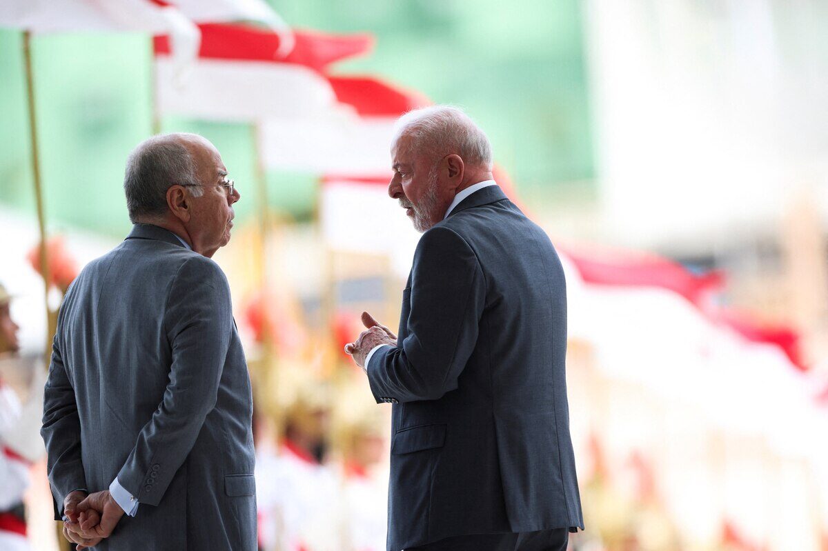 Dos hombres conversando en un evento oficial con banderas de fondo
