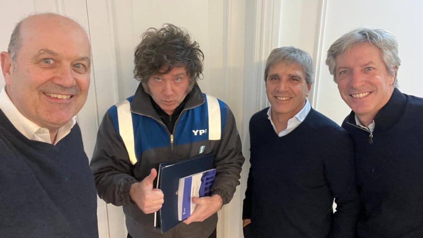 Cuatro hombres posando para una foto, uno de ellos sostiene un documento y muestra un pulgar hacia arriba