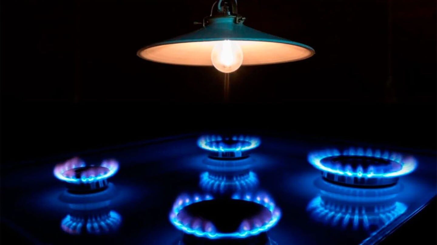 Lámpara encendida sobre una cocina de gas con llamas azules