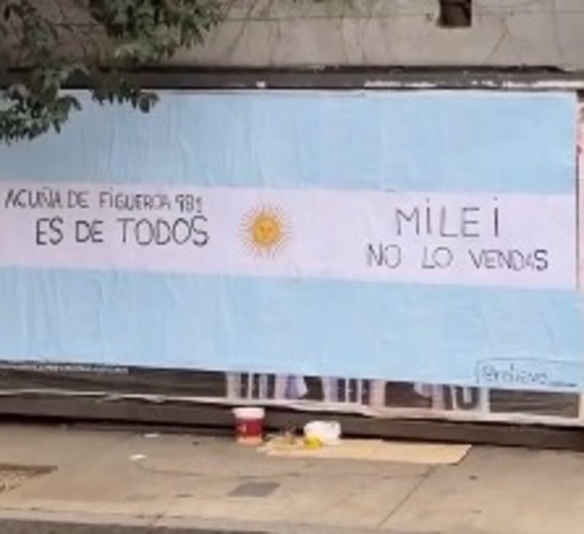 Pancarta en Acuña de Figueroa 981 que dice 'Milei no lo vendas' con fondo de bandera argentina