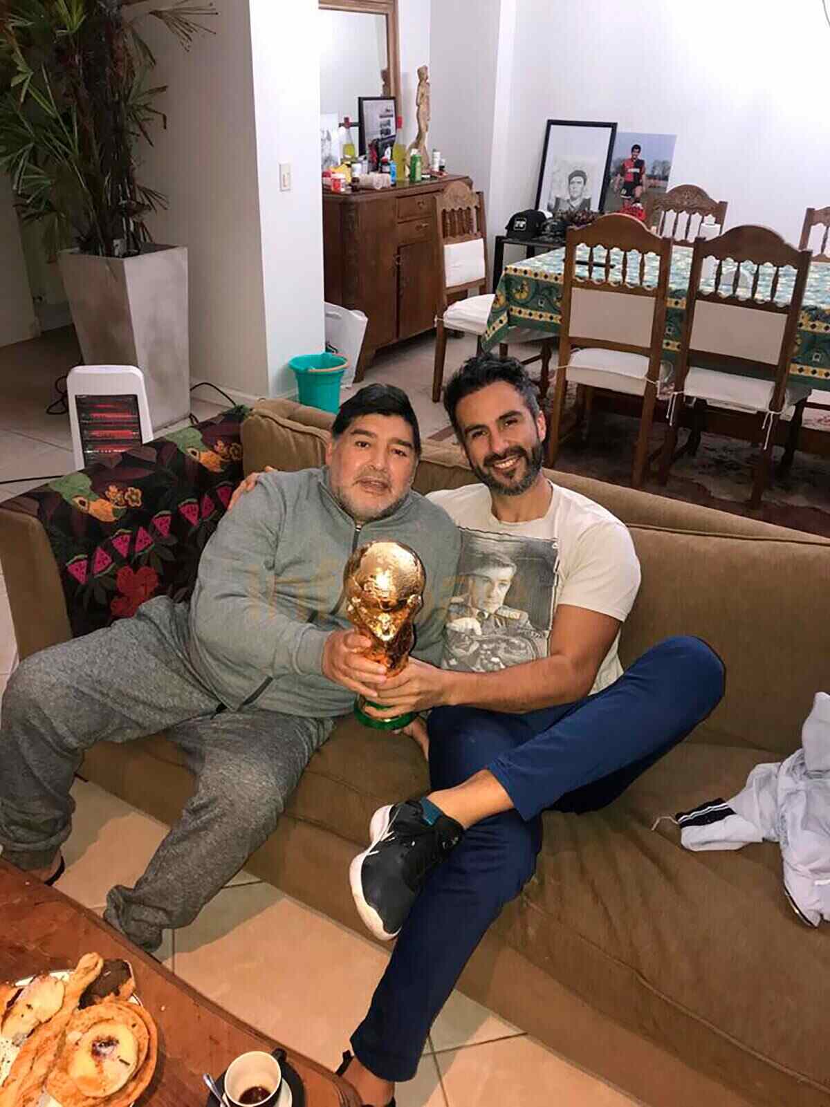 Luciano Spena y Diego Maradona sosteniendo la copa del mundo en un sofá