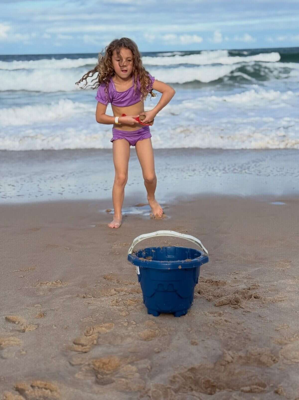 Niña jugando en la playa con un balde azul en la arena