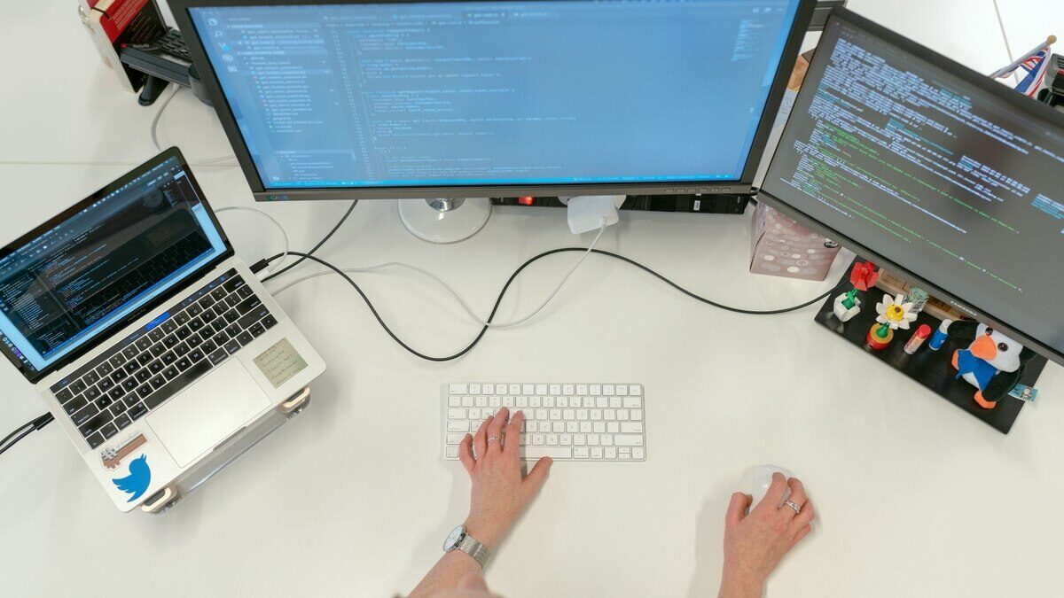 Persona trabajando en programación de software con dos monitores y un laptop