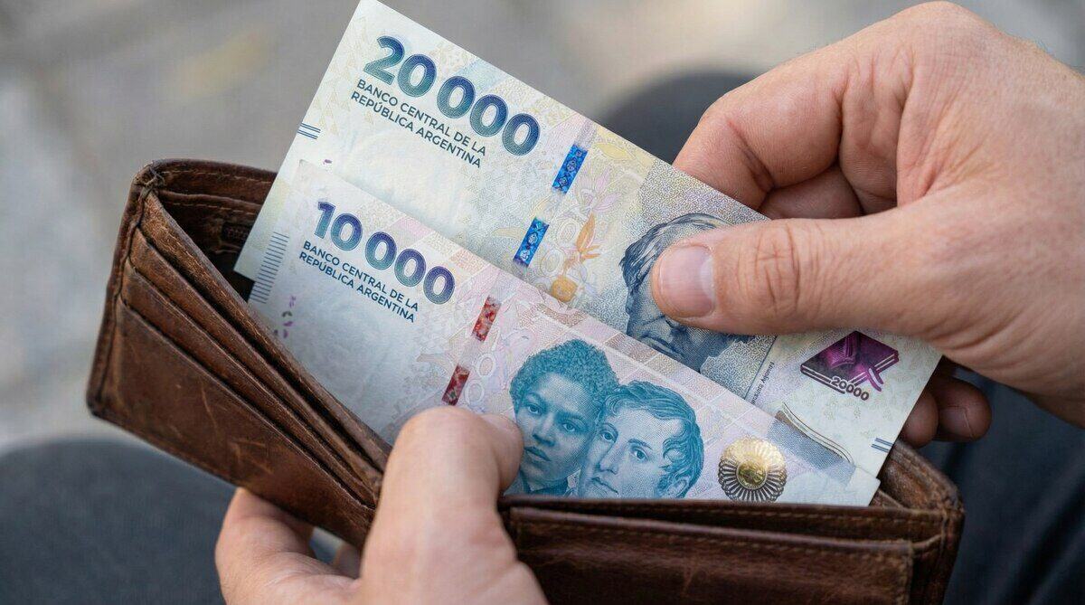 Mano sosteniendo billetes de 10,000 y 20,000 pesos argentinos en una billetera