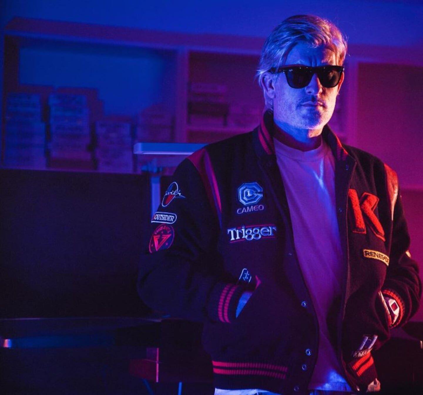 DJ francés Kavinsky con gafas de sol y chaqueta en un ambiente iluminado con luces de neón