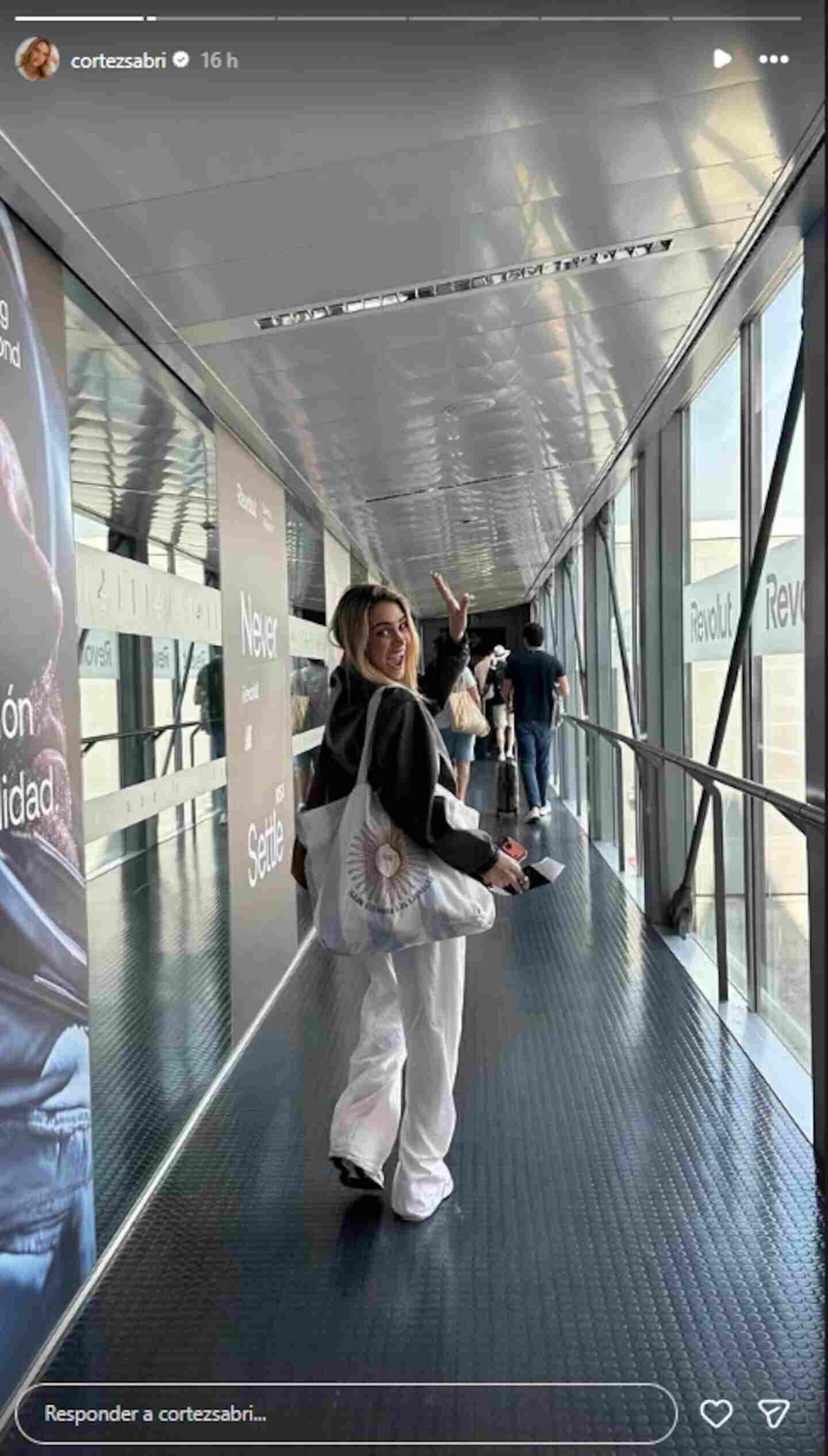 Sabrina Cortéz caminando por un pasillo en un aeropuerto con una sonrisa y saludando