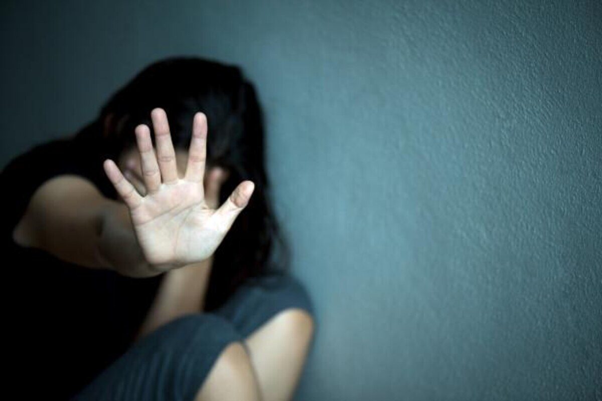 Mujer con la mano levantada en señal de rechazo, sentada contra una pared
