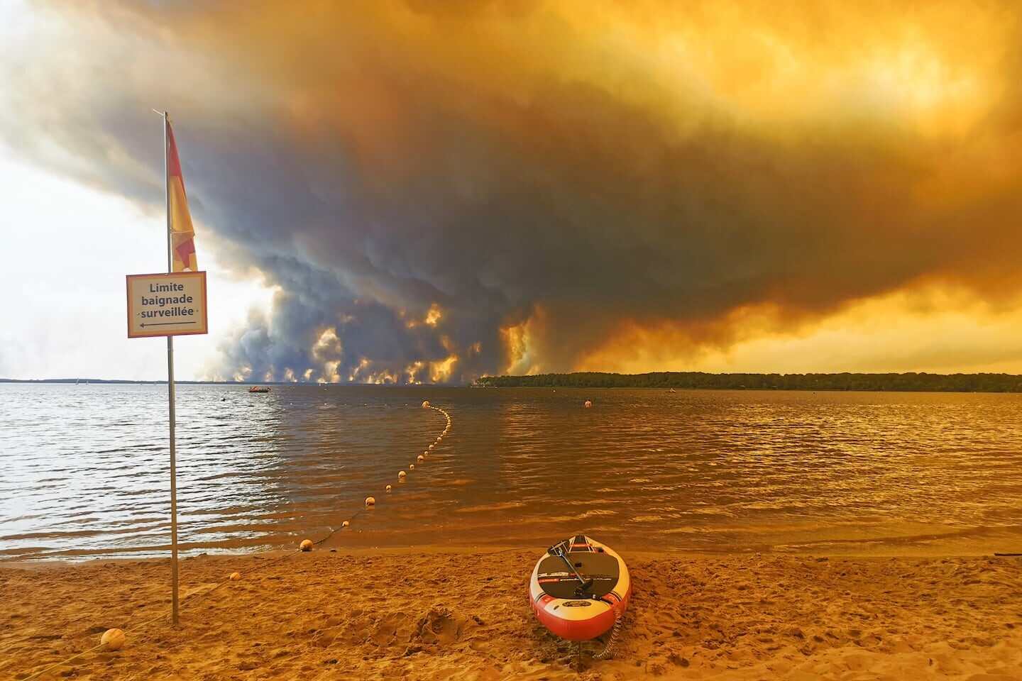 Incendios forestales en Francia visibles desde una playa con una tabla de paddle en la orilla