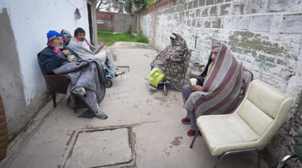 Adultos mayores sentados en un espacio exterior de un geriátrico clandestino en Santa Fe, cubiertos con mantas
