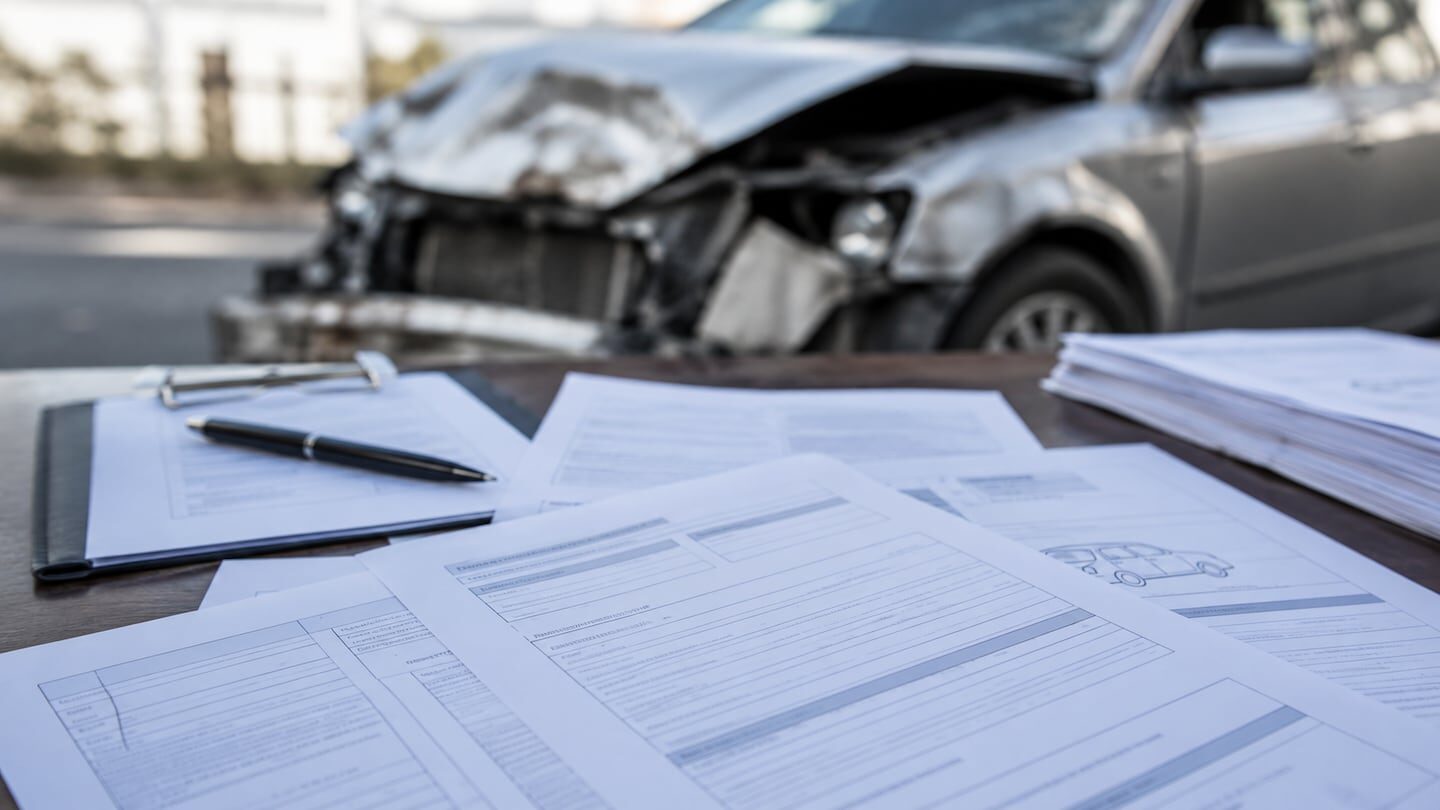Documentos de reclamación de indemnización sobre un accidente automovilístico frente a un coche dañado