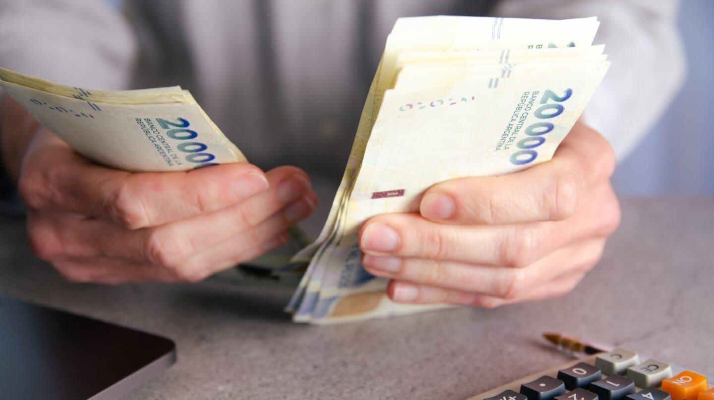 Persona contando billetes de 20,000 pesos en una mesa con una calculadora
