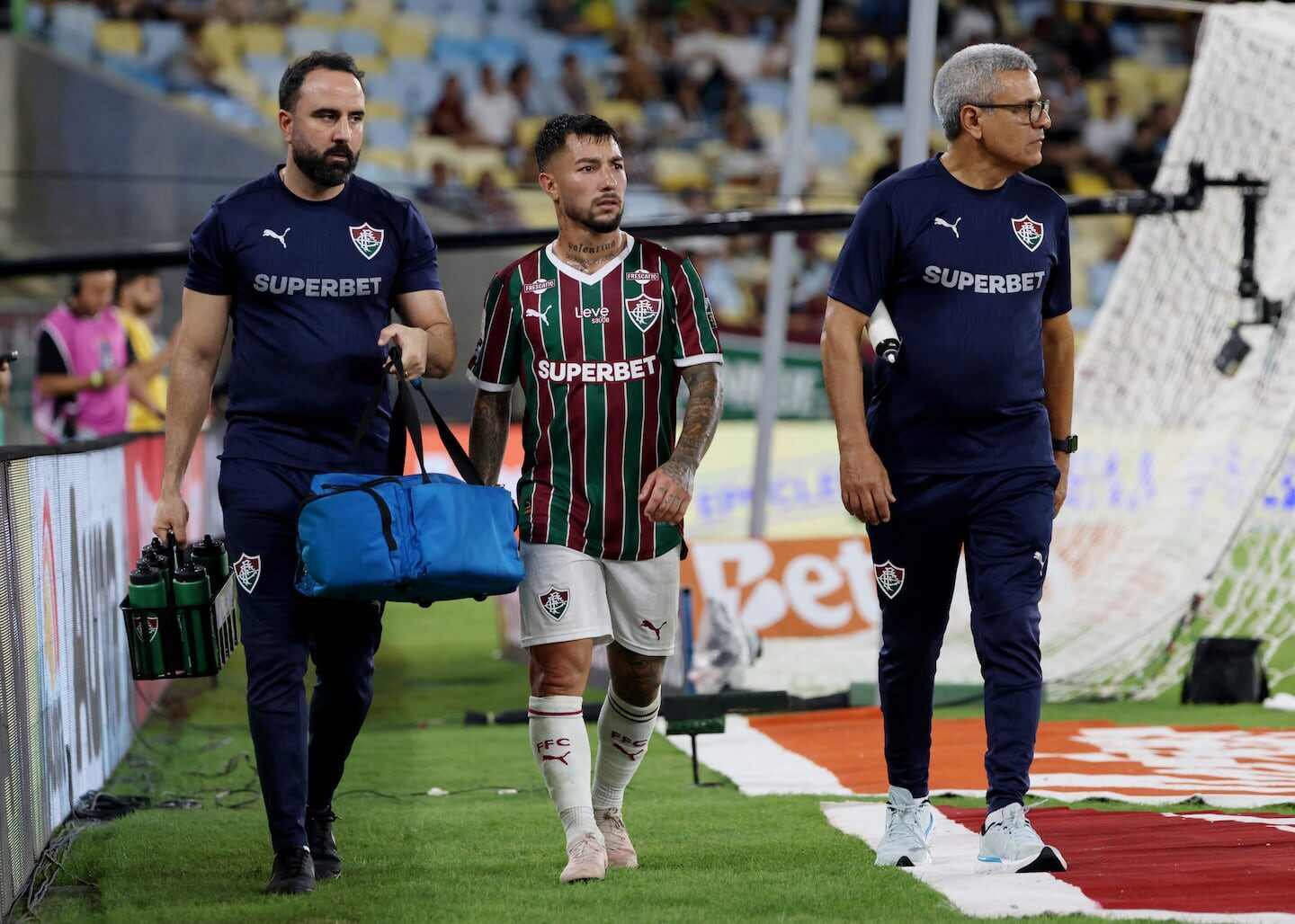 Luciano Acosta saliendo del campo acompañado por dos miembros del equipo médico del Fluminense