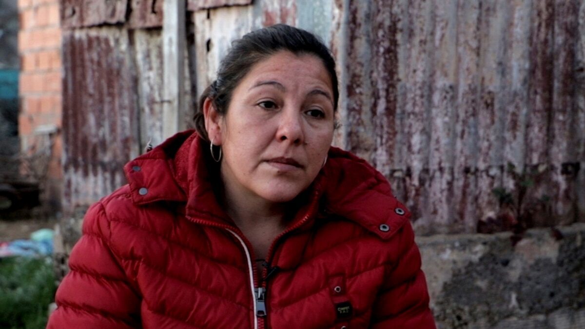 Mujer con chaqueta roja sentada frente a una pared deteriorada