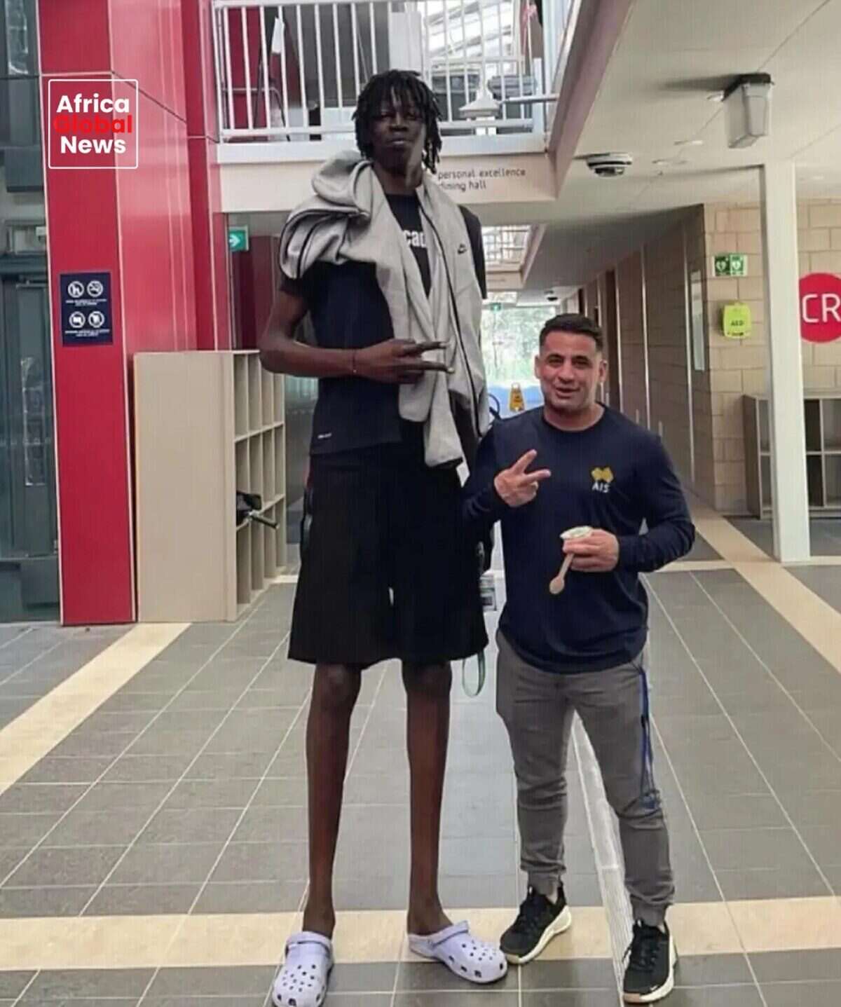 Jongkuch Mach, un joven jugador de básquet de casi 2.30 metros, posando junto a un hombre más bajo en un entorno urbano