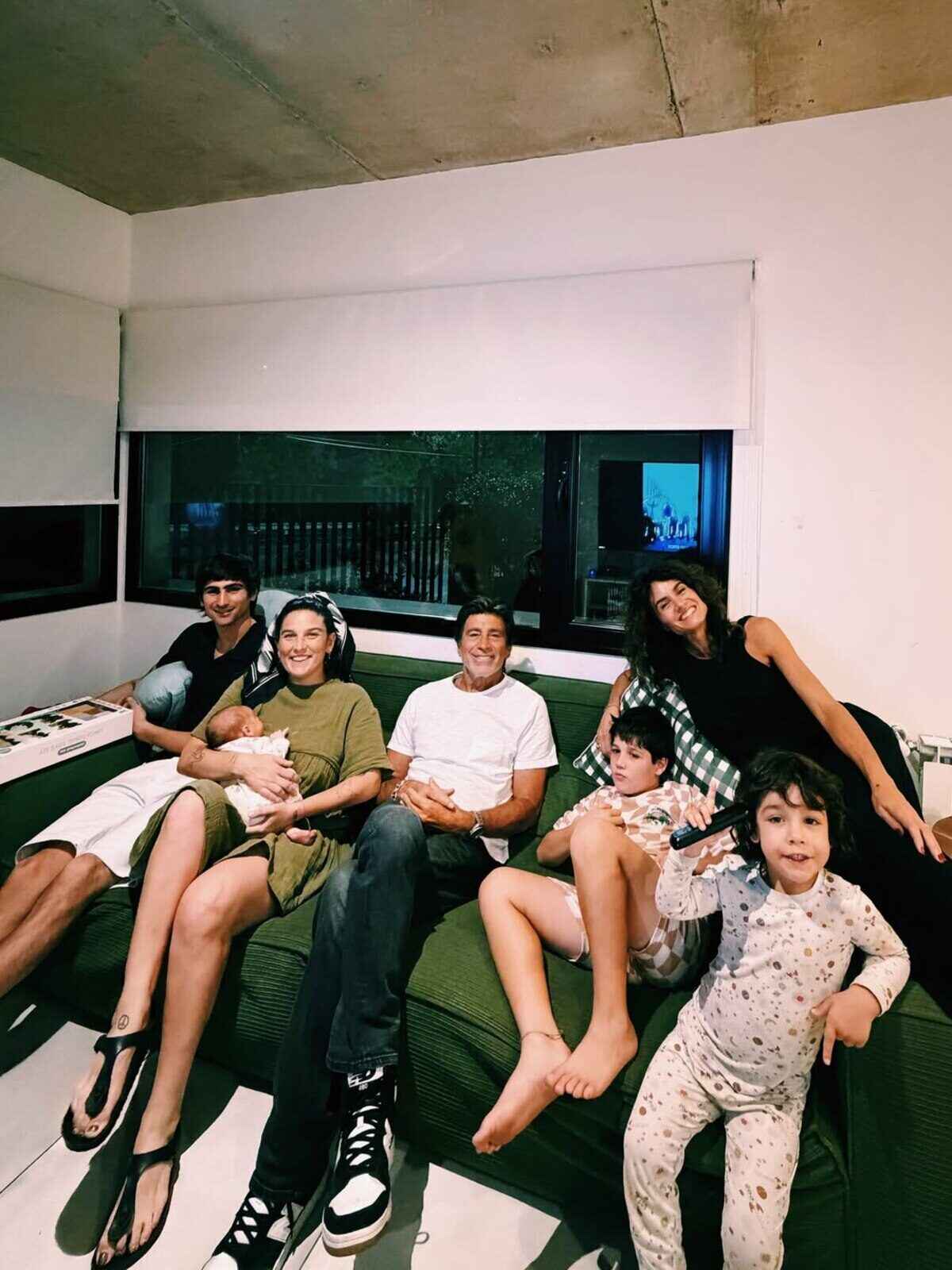Grupo de seis personas sentadas en un sofá, algunas con niños, en un ambiente acogedor
