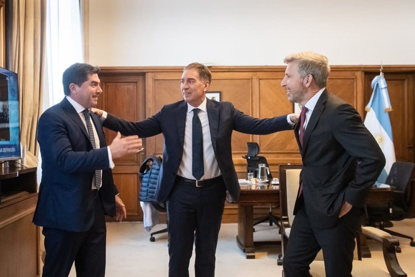 Tres hombres conversan en una oficina con decoración clásica, en un contexto político argentino
