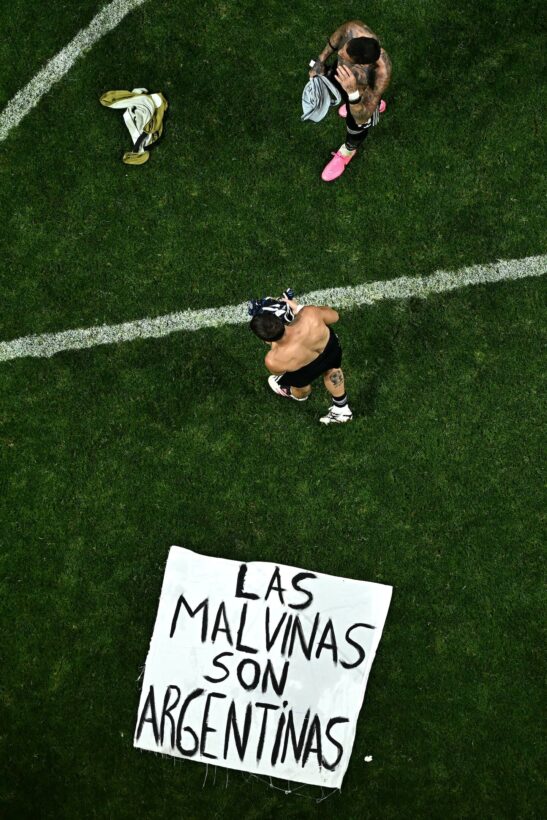 Jugadores de la Selección argentina sosteniendo una bandera que dice 'Las Malvinas son argentinas' en el campo de juego