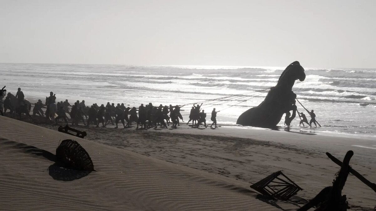 Grupo de personas arrastrando una gran figura de caballo en la playa