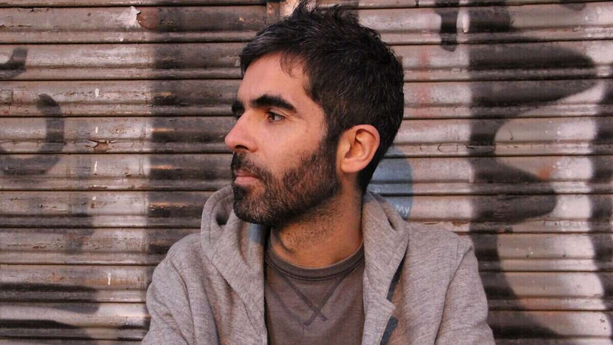 Retrato de un hombre con barba sentado frente a una pared con grafitis