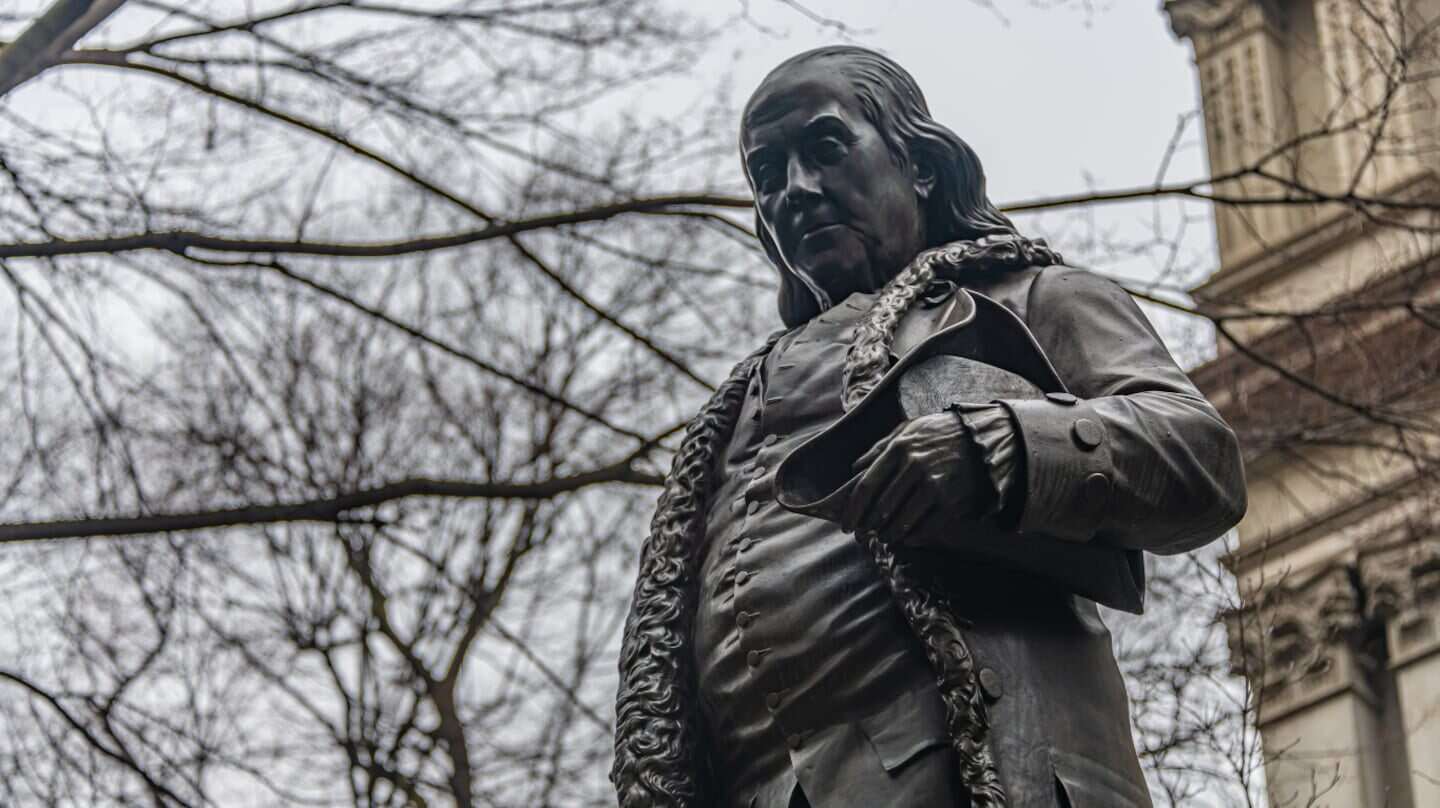 Estatua de Benjamin Franklin sosteniendo un libro en un entorno urbano